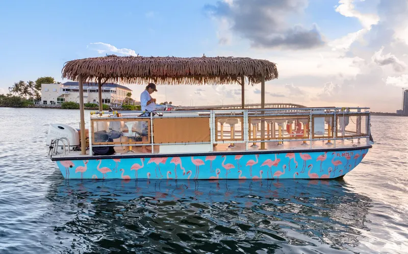 Slide: The Image of 2023 Beachcat 26 Tiki COI boat with flamingo design on calm water. - 2