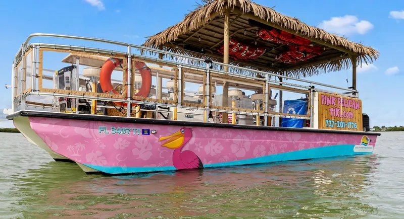 Slide: The Image of 2023 Beachcat 26 Tiki COI boat with pink hull and tiki-style roof on water. - 28
