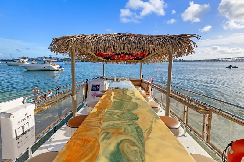 Slide: The Image of Tropical-themed Beachcat 26 Tiki COI boat with bar, 2023 model, on serene water. - 5
