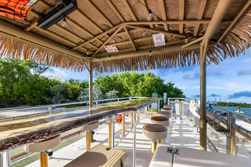 Slide: The Image of Tiki-themed boat deck with bar stools, lush greenery, and ocean view; Beachcat 26 Tiki COI 2023. - 7