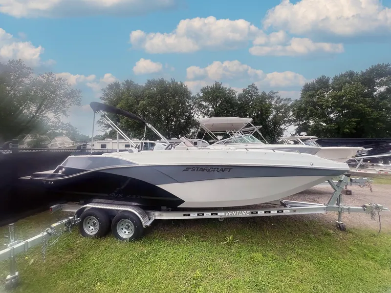 The Image of 2024 Starcraft SVX 231 OB DH boat on trailer, parked on grass under a blue sky. - 0