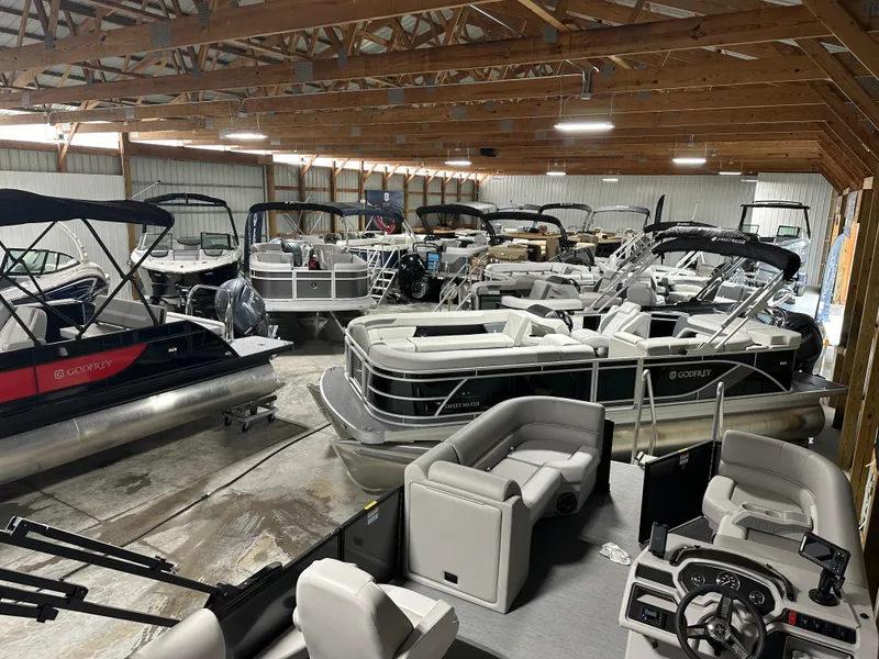 Slide: The Image of Indoor showroom displaying multiple 2025 Godfrey Xperience Lounge pontoon boats. - 17