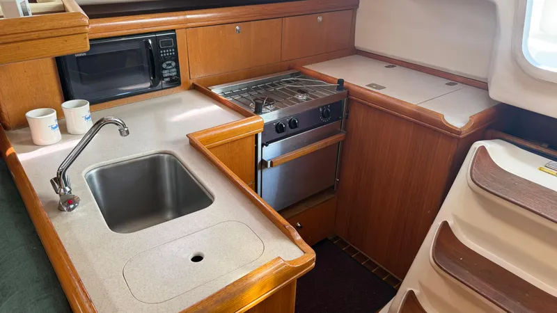 Slide: The Image of 2002 Hunter 326 yacht kitchen with sink, stove, microwave, and wooden cabinetry. - 14