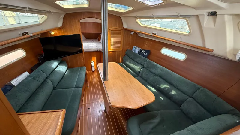 Slide: The Image of Interior of 2002 Hunter 326 sailboat with green seating, wooden table, and mounted TV. - 3