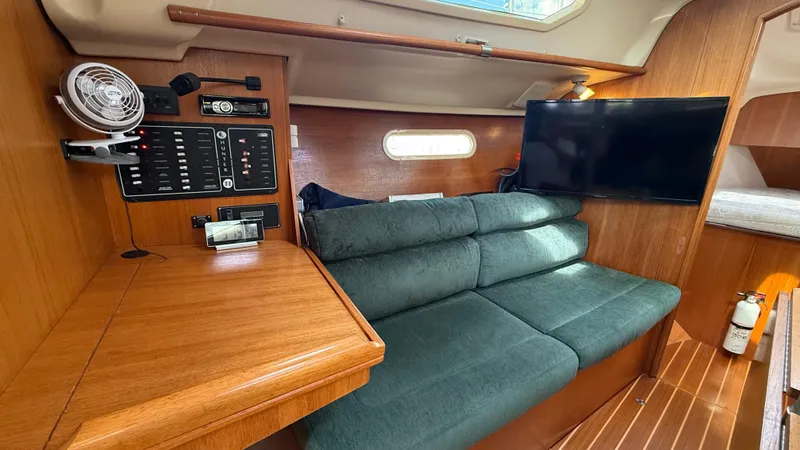 Slide: The Image of Interior of a 2002 Hunter 326 sailboat with green sofa, control panel, and mounted TV. - 7