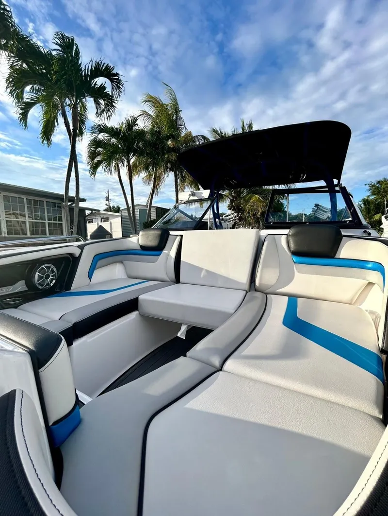 Slide: The Image of 2018 Yamaha Boats 242X E-Series interior with sleek seating, palm trees, and blue sky backdrop. - 14