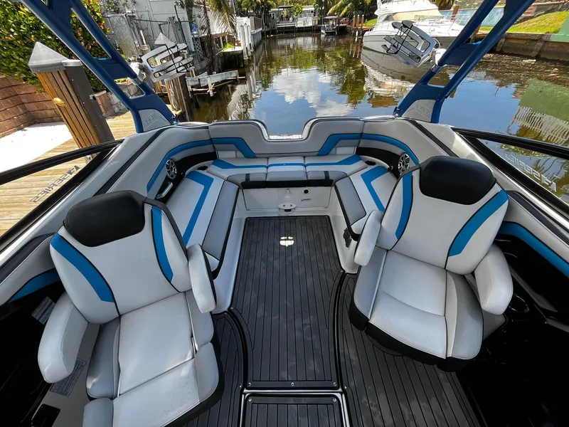 Slide: The Image of 2018 Yamaha Boats 242X E-Series interior with blue and white seating, docked by a canal. - 15