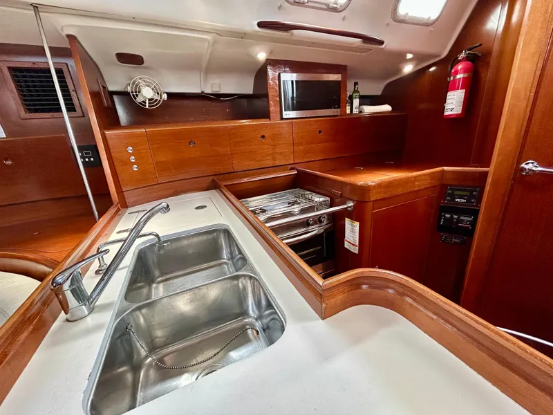 Slide: The Image of Beneteau First 47.7 2003 yacht kitchen with wooden cabinetry, stainless steel sink, and modern appliances. - 17