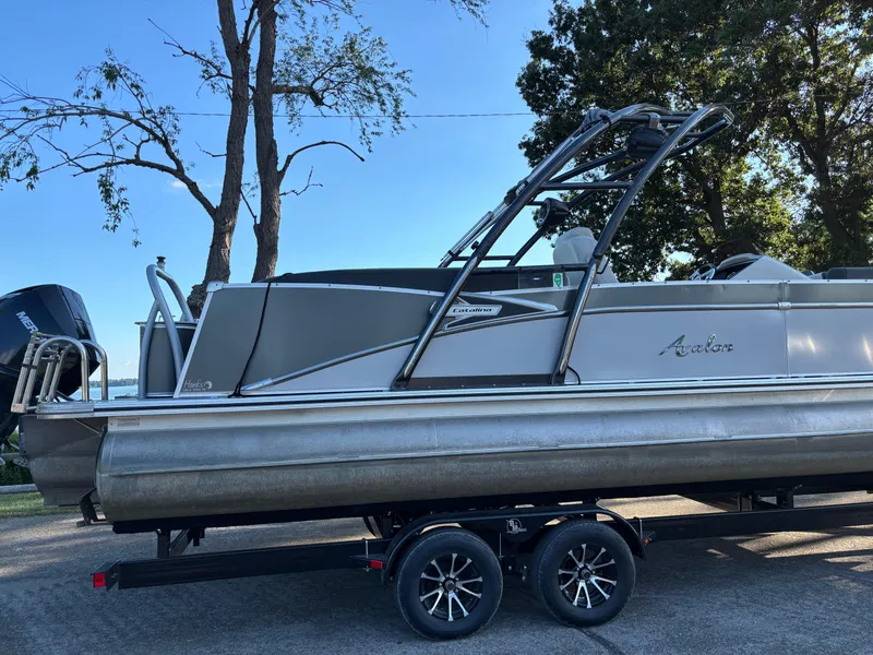 Slide: The Image of 2021 Avalon Catalina Entertainer 25' pontoon boat on trailer, parked near trees. - 1