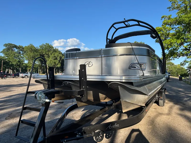 Slide: The Image of 2021 Avalon Catalina Entertainer 25' pontoon boat on trailer, parked outdoors under clear blue sky. - 2
