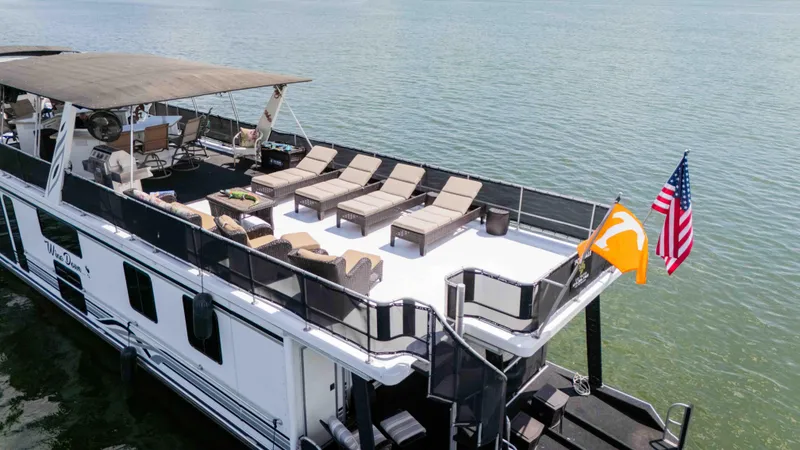 Slide: The Image of 1998 Sumerset houseboat with sun deck, lounge chairs, and flags on a calm lake. - 16