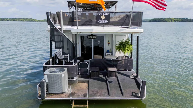 Slide: The Image of 1998 Sumerset houseboat for sale on a lake, featuring outdoor seating and American flag. - 17