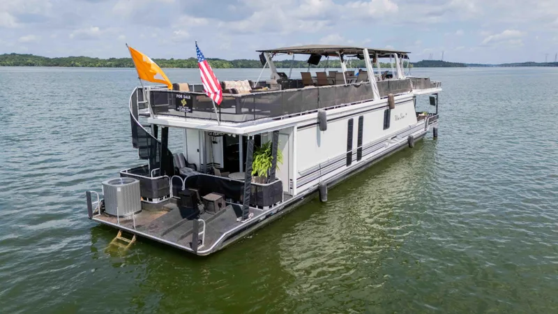 Slide: The Image of 1998 Sumerset houseboat on a lake, featuring upper deck seating and flags. - 18