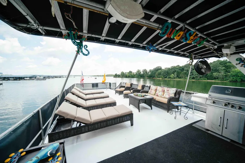 Slide: The Image of 1998 Sumerset houseboat deck with lounge chairs, seating area, and grill on a serene lake. - 23