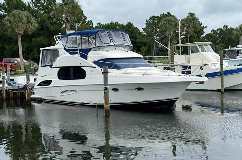Slide: The Image of 2002 Silverton 43 Motor Yacht docked in a marina, surrounded by trees and other boats. - 0