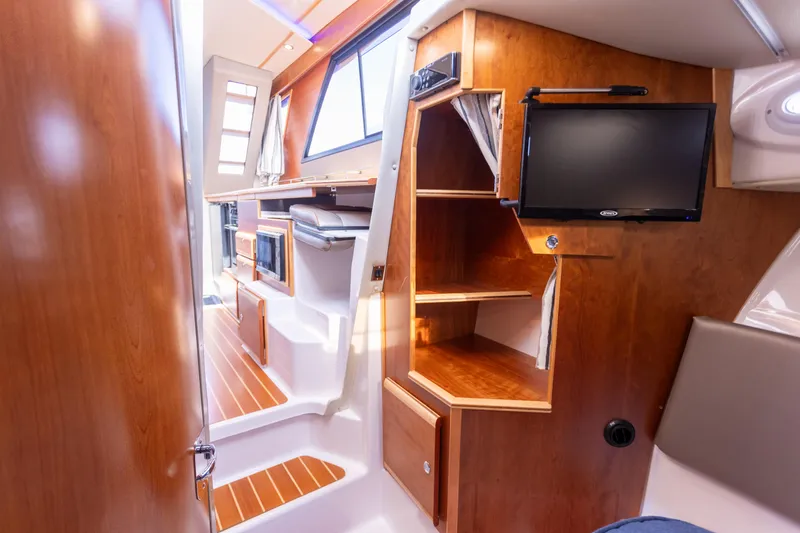 Slide: The Image of 2021 Cutwater C-32 CB interior with wood finish, shelves, and mounted TV. - 32