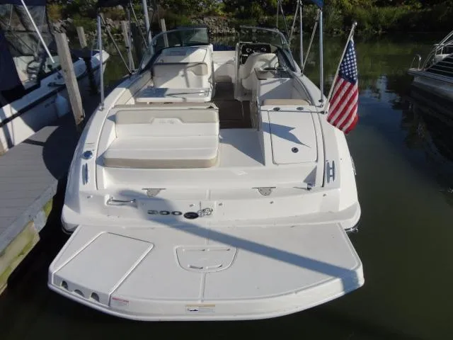 Slide: The Image of 2013 Sea Ray 300 Sundeck boat docked, featuring spacious deck and American flag. - 19