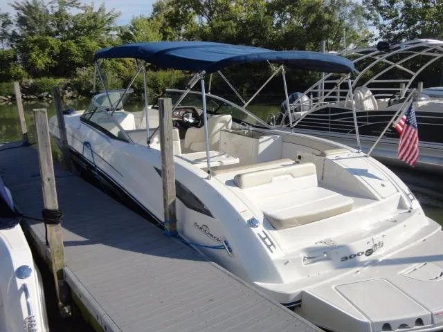 Slide: The Image of 2013 Sea Ray 300 Sundeck boat docked, featuring a blue canopy and American flag. - 20