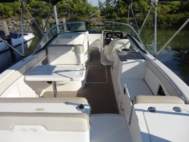 Slide: The Image of 2013 Sea Ray 300 Sundeck boat interior with seating and table, docked by greenery. - 21