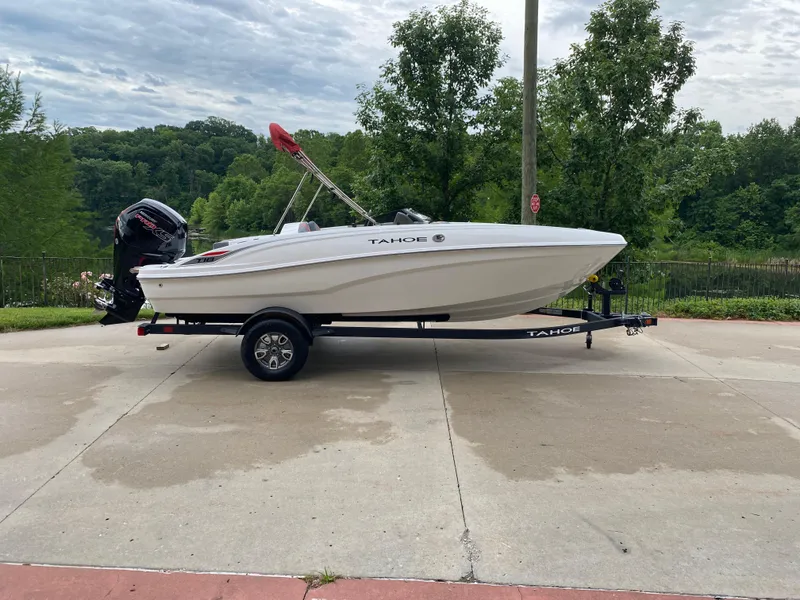 Slide: The Image of 2025 Tahoe T18 boat on trailer, parked outdoors with lush greenery background. - 0
