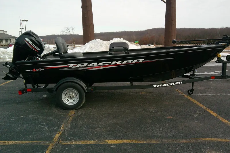 The Image of 2025 Tracker Super Guide V-16 T boat on trailer, black with Mercury engine, parked outdoors. - 0