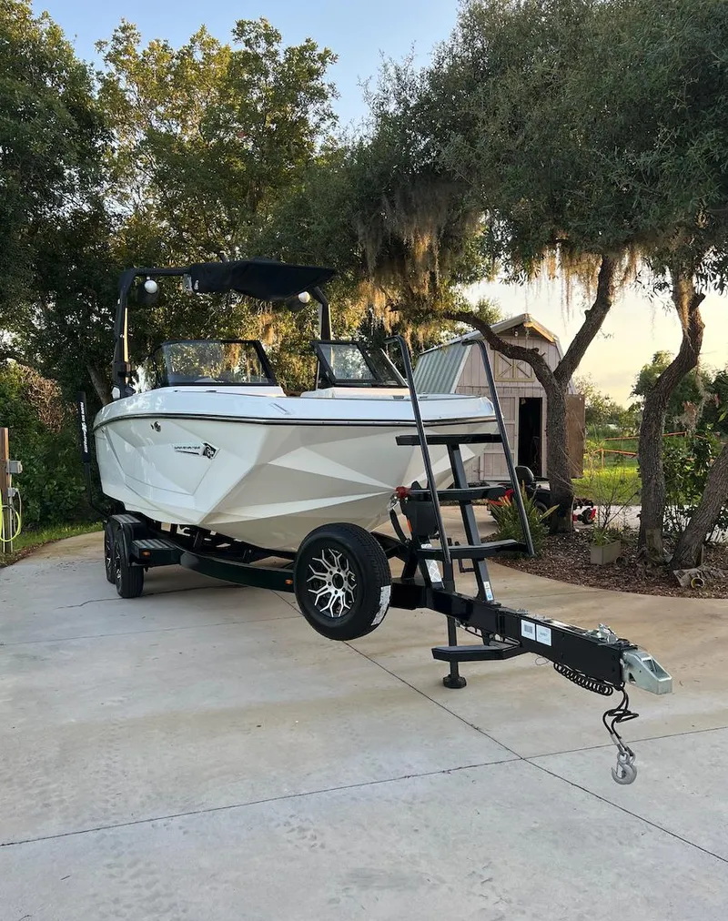 Slide: The Image of 2022 Nautique Super Air G23 boat on trailer, parked outdoors near trees. - 1