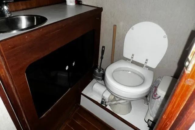 Slide: The Image of 1985 Bayliner 3870 Motoryacht bathroom with toilet and sink, featuring wooden cabinetry. - 20