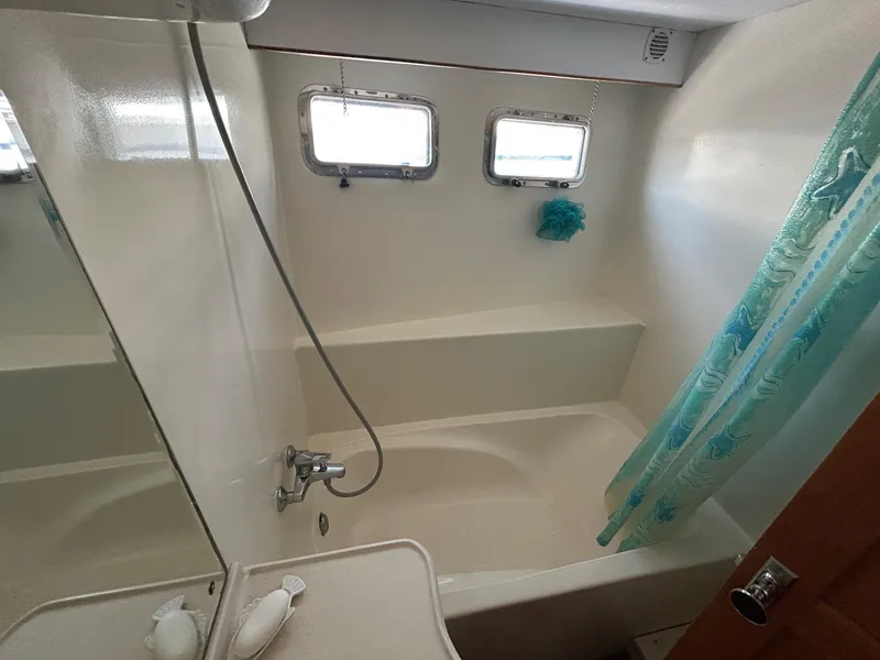 Slide: The Image of Bathroom with shower and tub in 1999 Selene 43 yacht, featuring porthole windows and blue shower curtain. - 33