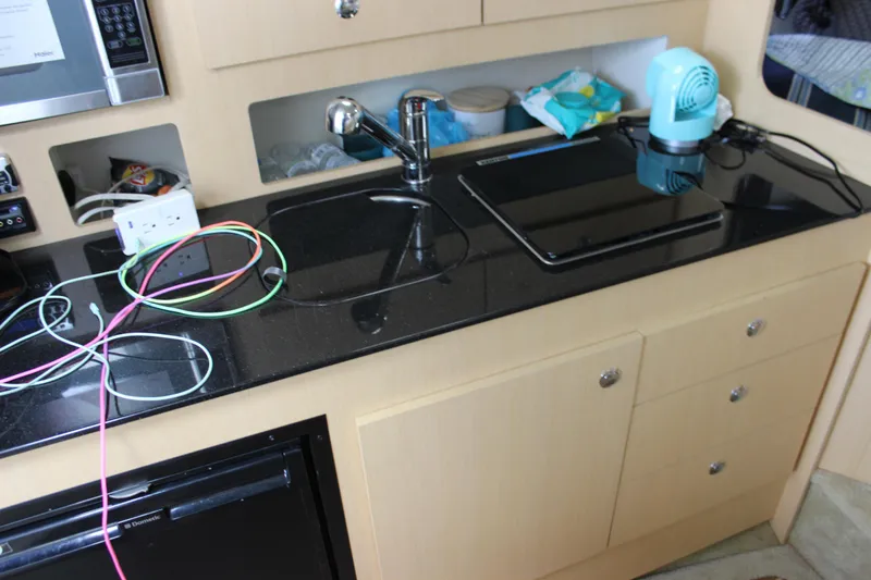 Slide: The Image of 2012 Bayliner 315 Cruiser kitchen with black countertop, sink, and stove. - 23