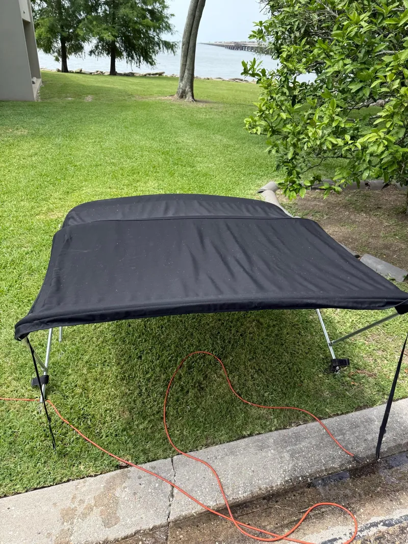 Slide: The Image of Black bimini top for 2011 Bayliner 184 SF on grassy area near water. - 6