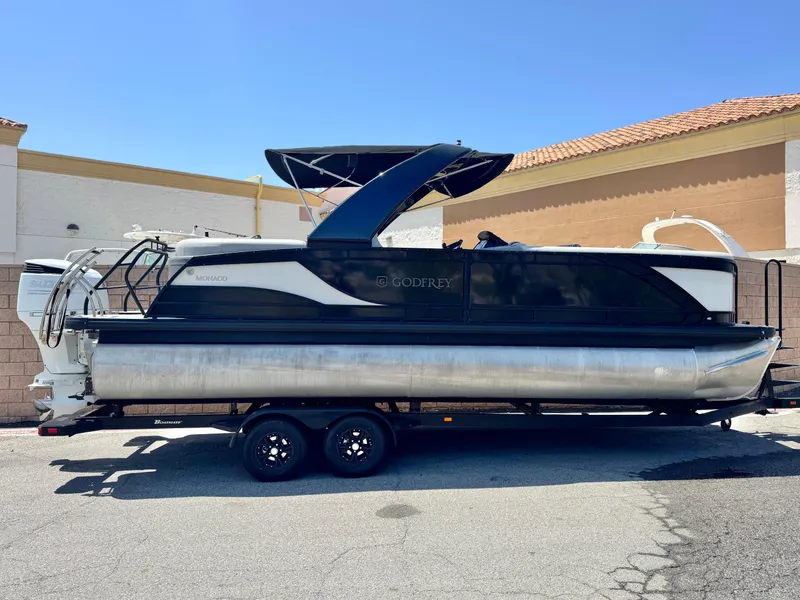 The Image of 2023 Godfrey Monaco 255 C pontoon boat on trailer, parked outdoors. - 0