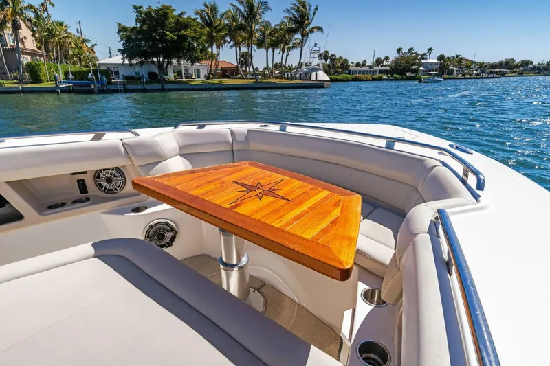 Slide: The Image of 2019 Boston Whaler 350 Realm boat interior with wooden table, docked by palm trees. - 14