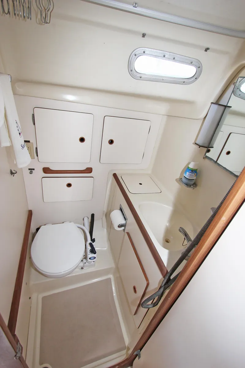 Slide: The Image of 1977 Pearson 10M sailboat bathroom with compact design, white cabinetry, and porthole window. - 11
