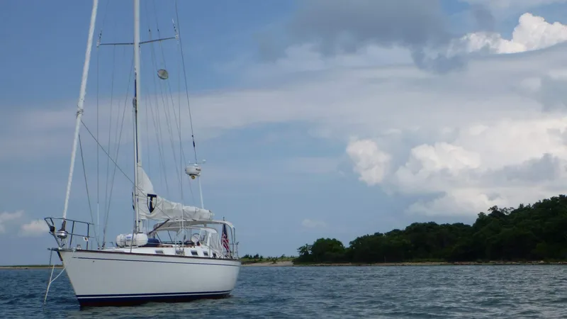 Slide: The Image of Sailboat Tartan 40CB 1987 on calm waters near a lush shoreline under a cloudy sky. - 4