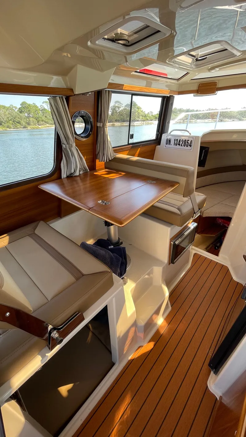 Slide: The Image of 2022 Ranger Tugs R-25 interior with wood accents and seating, overlooking water. - 12