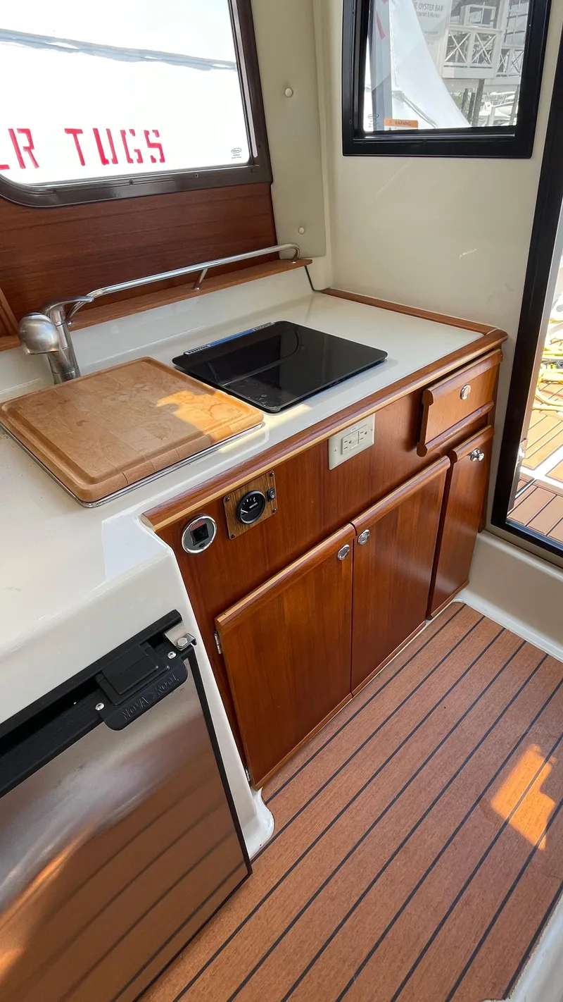 Slide: The Image of 2022 Ranger Tugs R-25 interior kitchen with sink, wooden cabinetry, and cutting board. - 28