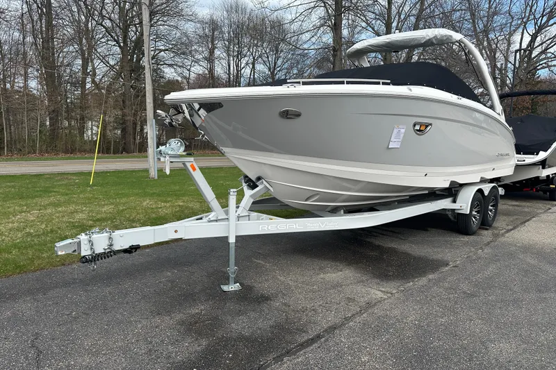 Slide: The Image of 2026 Regal LS9 boat on trailer, parked on pavement near grassy area and trees. - 1
