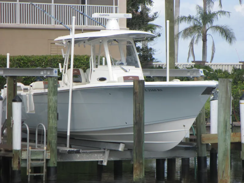 The Image of 2018 Cobia 301 Center Console boat docked near waterfront buildings under clear blue sky. - 0