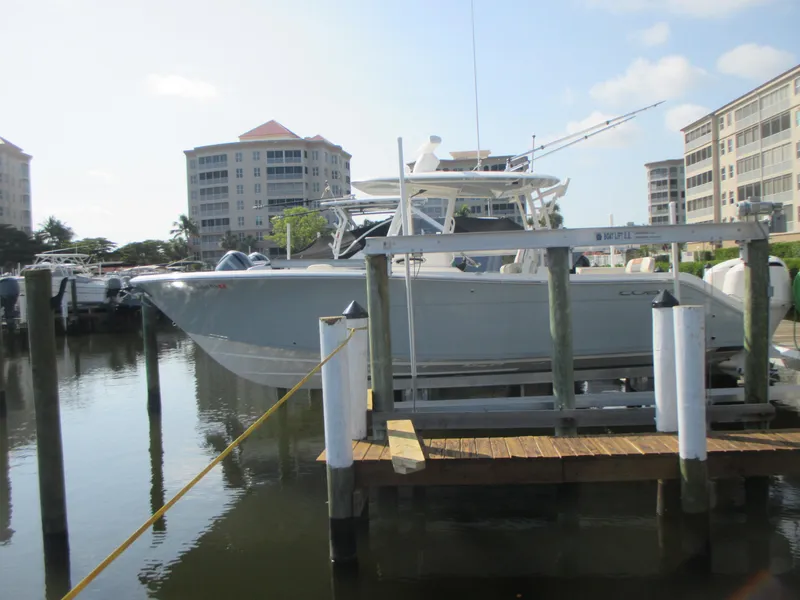 Slide: The Image of 2018 Cobia 301 Center Console boat docked on a lift by the water. - 2