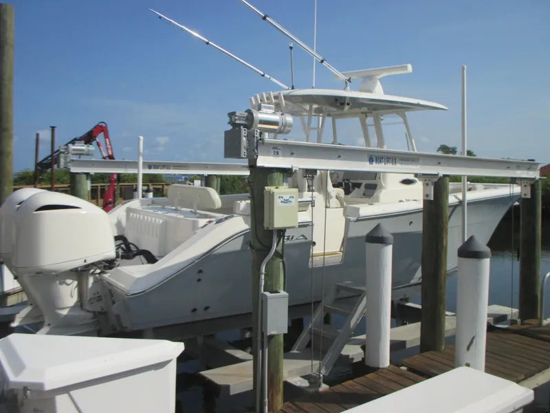 Slide: The Image of 2018 Cobia 301 Center Console boat docked on a lift under clear blue skies. - 3