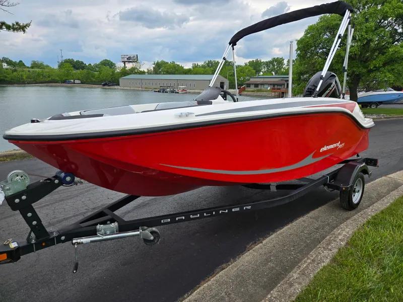 Slide: The Image of 2022 Bayliner Element M15 boat in vibrant red on a trailer by a lakeside road. - 8