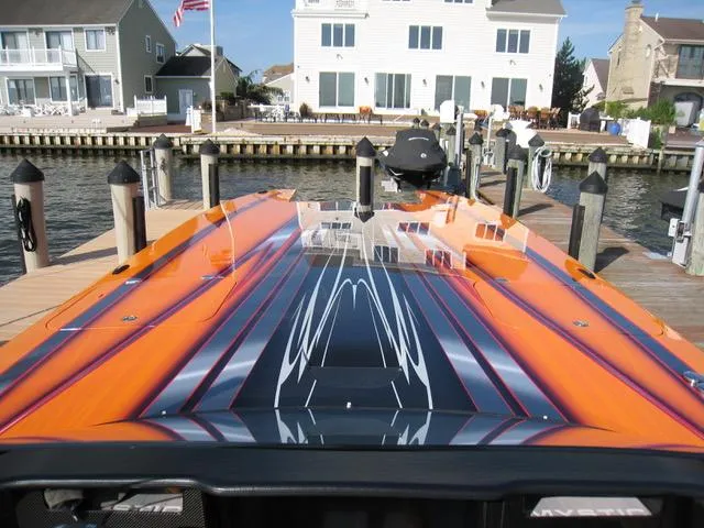 Slide: The Image of 2024 Mystic Powerboats C4000 with vibrant orange and black design docked by waterfront homes. - 3