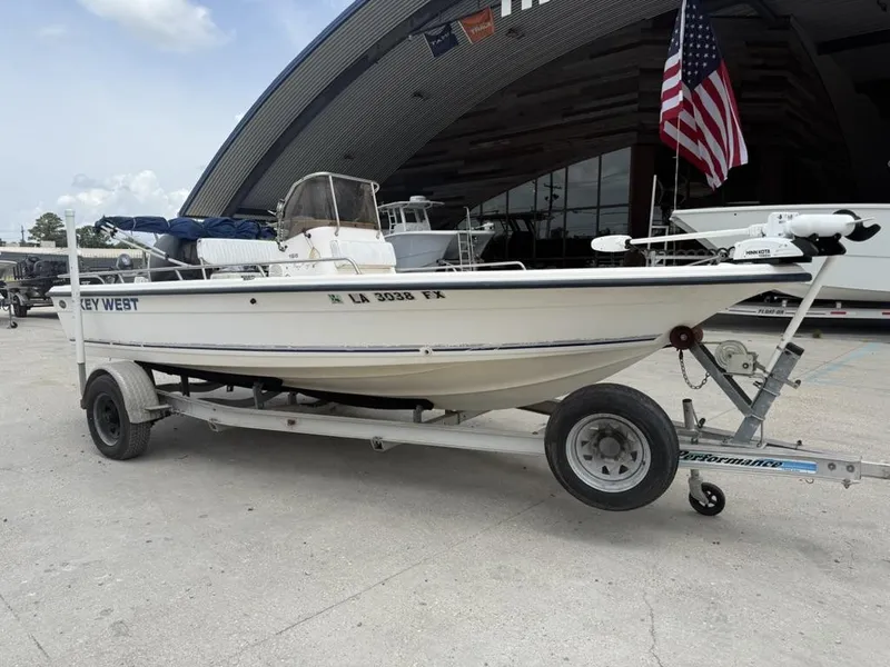 Slide: The Image of 2001 Key West 196 Bay Reef boat on trailer, parked near a large building with American flag. - 12