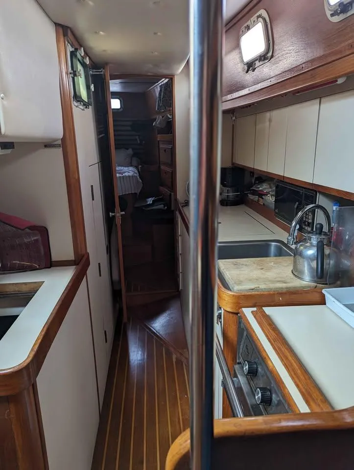 Slide: The Image of Interior of 1985 Endeavour 42 CC sailboat, featuring a compact kitchen and wooden flooring. - 3