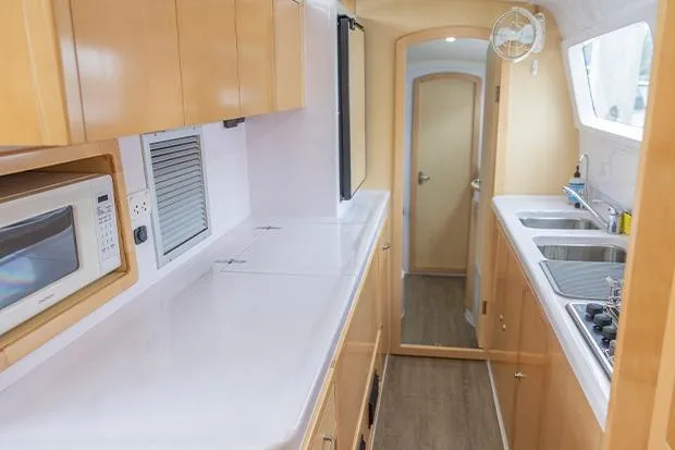 Slide: The Image of 2019 Seawind 1260 yacht interior kitchen with wooden cabinets, microwave, and dual sinks. - 19