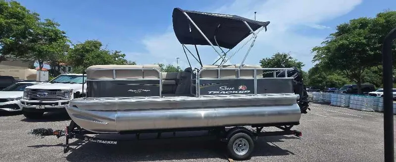 The Image of 2025 Sun Tracker Party Barge 18 DLX pontoon boat on trailer, parked outdoors. - 0