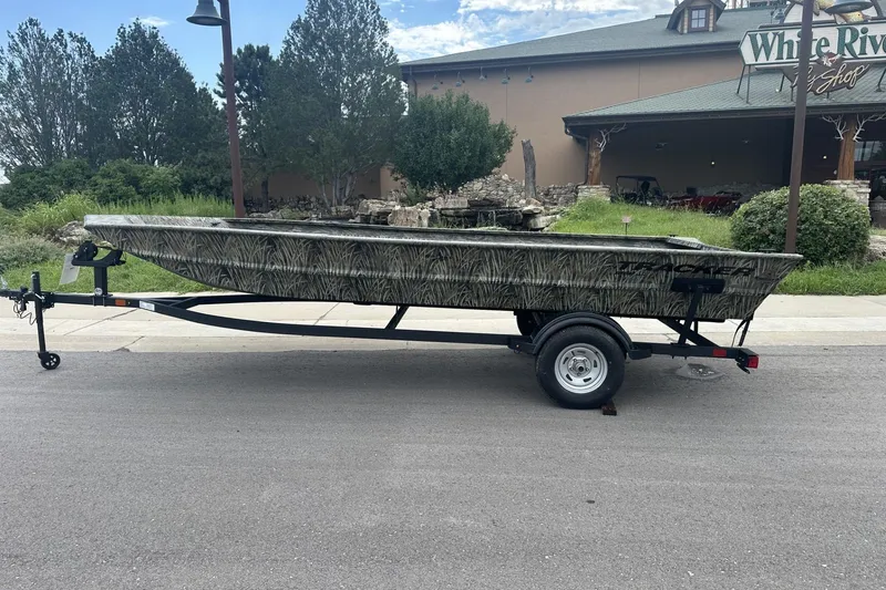 The Image of 2025 Tracker Grizzly 1860 Utility boat on trailer, parked outdoors near a shop. - 0