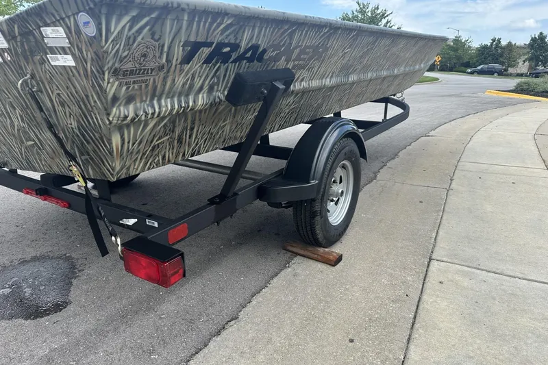 Slide: The Image of 2025 Tracker Grizzly 1860 Utility boat on trailer, parked on a street. - 3