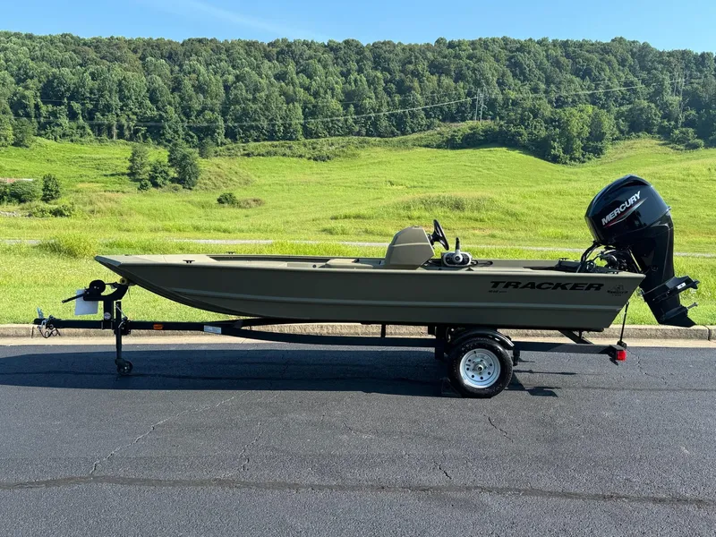 The Image of 2025 Tracker Grizzly 1648 SC boat on trailer, parked on asphalt with green hills in background. - 0