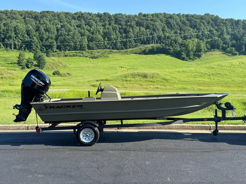 Slide: The Image of 2025 Tracker Grizzly 1648 SC boat on trailer, parked on asphalt with green hills in background. - 2